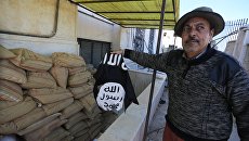 Житель Сирии держит флаг группировки Исламское государство. Архивное фото Житель Сирии держит флаг группировки Исламское государство. Архивное фото